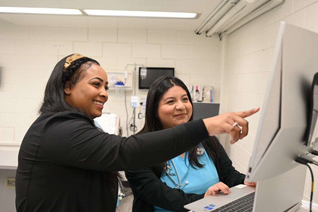 Hispanic nursing students in class observing readings on computer monitor.
