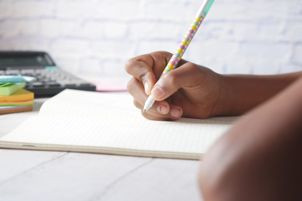 Child girl hand writing on notepad sitting on a chair