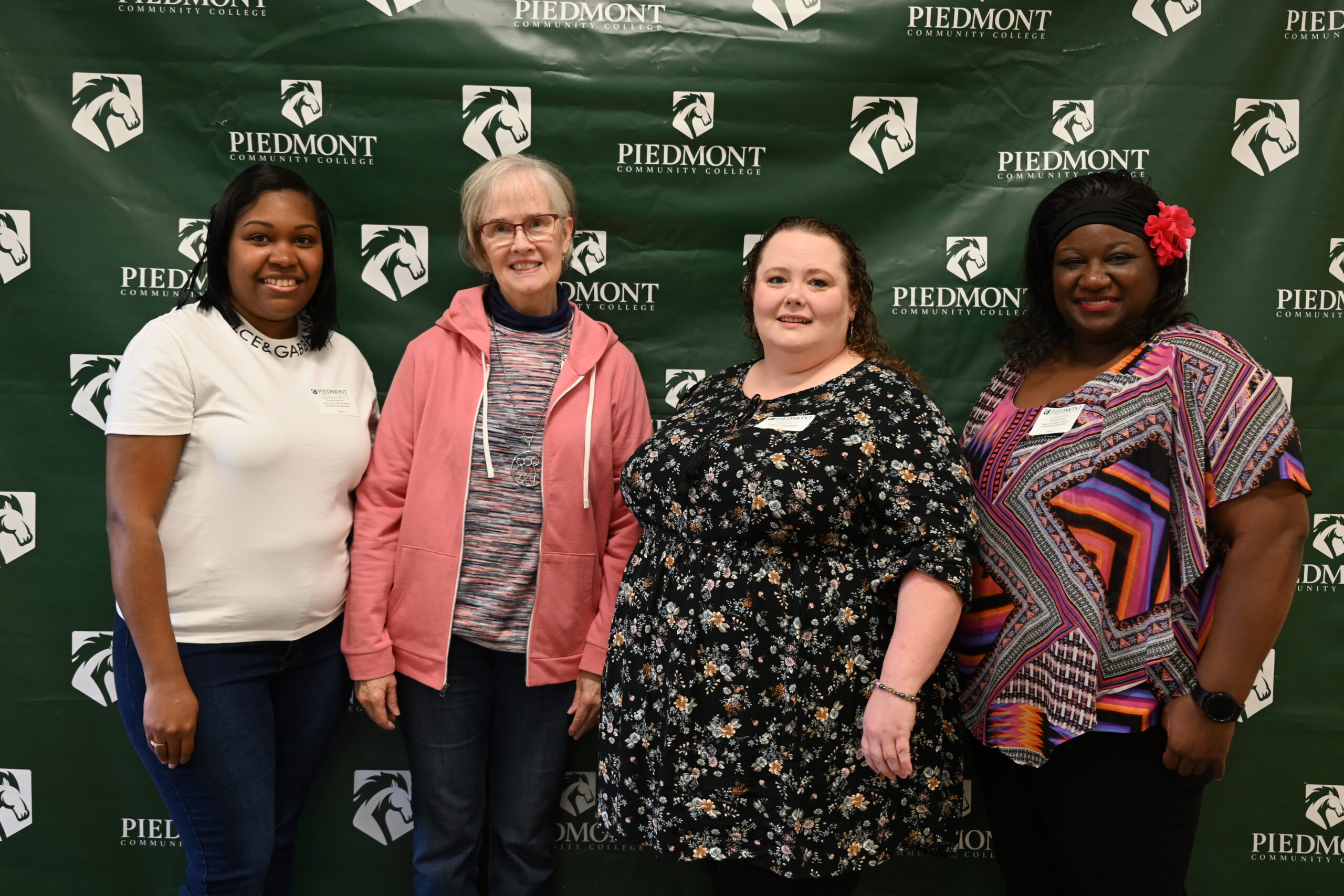 Four people posed in front of PCC branded backdrop
